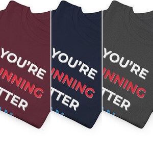 Pu&ograve; includere: Tre magliette in diversi colori: bordeaux, blu navy e grigio antracite. Ogni maglietta mostra il testo "YOU'RE WINNING BETTER" in lettere bianche e rosse. Le magliette sono piegate, mostrando il testo in modo prominente.