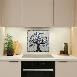 May include: A mosaic tile artwork depicting a tree with a dark blue trunk and branches, filled with green and blue leaves. The artwork is mounted on a kitchen backsplash. The kitchen has light-colored cabinets and a countertop.