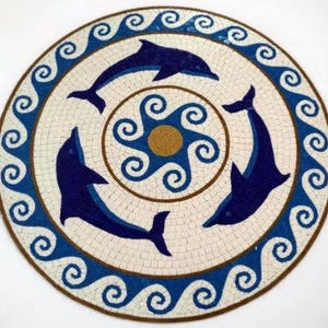 Puede incluir: Baldosa de mosaico redonda con tres delfines azul marino en un patrón circular. El diseño incluye un borde de olas azules y un motivo central con un centro dorado. La baldosa está hecha de pequeñas baldosas blancas y marrones.