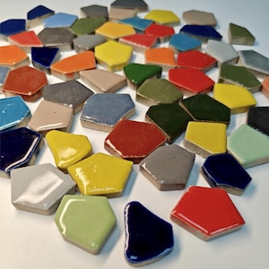 Puede incluir: Una colección de azulejos de cerámica coloridos de forma irregular en varios colores, incluyendo rojo, amarillo, azul, verde y gris. Los azulejos tienen un acabado brillante y están dispuestos sobre una superficie blanca. Adecuado para proyectos de arte de mosaicos.