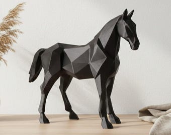 May include: A black geometric horse sculpture with a modern design. The sculpture is displayed on a wooden surface, next to a vase with dried plants. The horse has a faceted appearance, giving it a contemporary look.