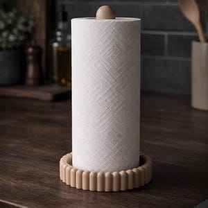 Puede incluir: Un soporte vertical para papel de cocina con una base circular estriada en color beige claro y un remate esf&eacute;rico a juego en la parte superior. El soporte contiene un rollo de papel blanco con un patr&oacute;n geom&eacute;trico en relieve.