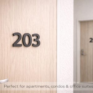 May include: A close-up of a wooden door with the number "203" in dark gray. A silver door handle is on the left. In the background, another door with the number "202" is visible.