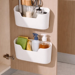 Può includere: Due cestini portaoggetti in plastica bianca montati su una porta di un armadio in legno. Il cestino superiore contiene utensili da cucina e spezie. Il cestino inferiore contiene prodotti per la pulizia, tra cui un flacone spray e un dosatore di sapone. L'anta dell'armadio è aperta.