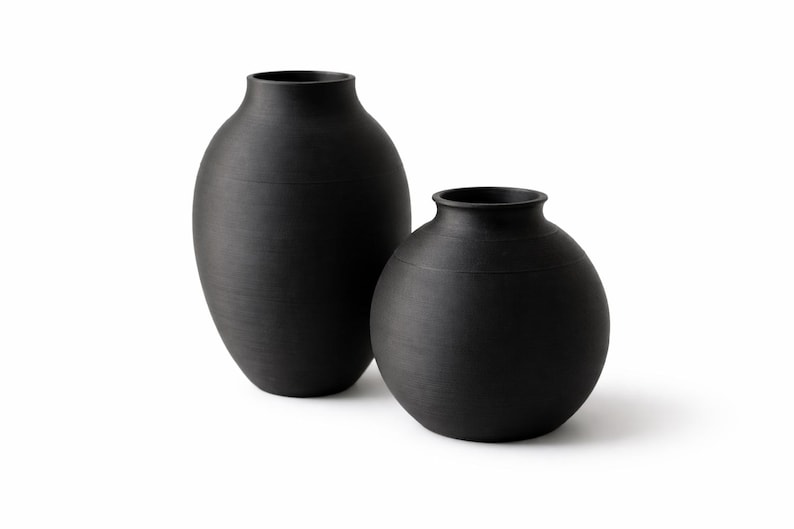 Pu&ograve; includere: Due vasi in ceramica neri. Uno &egrave; alto e di forma ovale, l'altro &egrave; rotondo. Entrambi hanno una finitura opaca e un design semplice ed elegante. I vasi sono adatti per l'arredamento della casa e composizioni floreali.