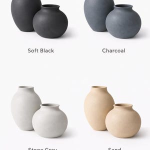 Pu&ograve; includere: Quattro coppie di vasi in ceramica in vari colori: nero morbido, carbone, grigio pietra e sabbia. Ogni coppia include un vaso pi&ugrave; grande e uno pi&ugrave; piccolo, di forma arrotondata e con collo stretto. I vasi sono esposti su sfondo bianco.
