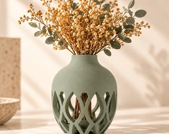 Può includere: Un vaso verde salvia con un corpo largo e arrotondato e un motivo geometrico a reticolo aperto attorno alla base. Il vaso è riempito con un bouquet di rametti secchi marrone chiaro e piccole foglie rotonde di colore verde opaco.