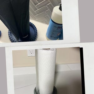Puede incluir: Un rollo de papel de cocina reutilizable con tela gris oscuro por fuera y blanca por dentro, sostenido por una base circular azul. Una segunda imagen muestra un rollo de papel blanco sobre una base circular gris junto a un jab&oacute;n.