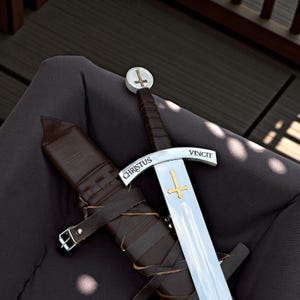 May include: A medieval sword with a silver blade and a brown leather-wrapped handle. The sword features the inscription "CHRISTUS VINCIT" and a gold cross design. A brown leather sheath rests beside the sword.