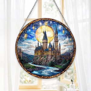 May include: A circular stained glass suncatcher featuring a detailed depiction of a castle at night under a large yellow moon. The scene includes a flowing river, dark blue starry sky, and hanging lanterns, all framed by a metal border with a chain.