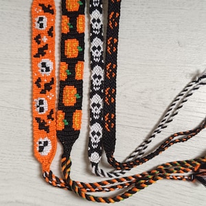 May include: Four handmade friendship bracelets with Halloween themes. The bracelets feature orange, black, and white patterns of skulls, bats, and pumpkins. The bracelets are made of woven thread and have braided ties.