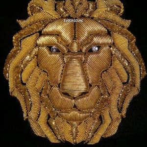 May include: A golden lion head design with a crown, made of intricately woven metallic threads. The lion's eyes are embellished with sparkling gemstones. The design is set against a black background, with the text "EVOCHICMC" visible.