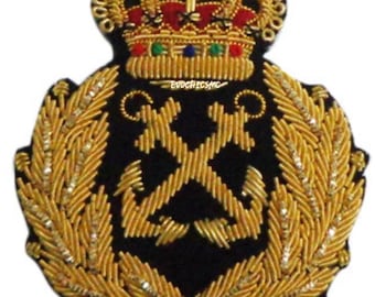 May include: A black embroidered patch featuring a gold crown with red and green accents at the top, positioned above two crossed gold anchors. The design is framed by two gold laurel branches and includes the text EVOCHICSMC in small gold letters.