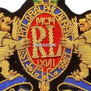 May include: A black embroidered patch featuring two gold lions standing on either side of a central red oval shield. The shield displays the letters RL, the Roman numerals MCMLXVII, and the text POLO RALPH LAUREN. The design includes blue accents.
