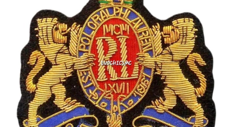 May include: A black embroidered patch featuring two gold lions standing on either side of a central red oval shield. The shield displays the letters RL, the Roman numerals MCMLXVII, and the text POLO RALPH LAUREN. The design includes blue accents.