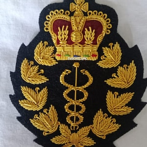 May include: Black felt patch with gold and red embroidery. Features a crown, caduceus, and leaf designs. The text "EVOCHICSMCI" is visible. This patch is likely for a uniform or decorative item.