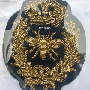 May include: A black fabric patch featuring gold bullion embroidery of a bee centred within a laurel wreath, topped with a crown. The text EVOCHICSMC is embroidered in small gold letters between the crown and the bee, creating a detailed emblem.