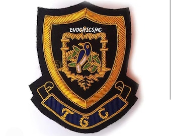 May include: A black and gold embroidered patch in a shield shape. The patch features a central design of a bird and foliage, with the text "EVOGHICMC" at the top and "TGC" on a blue banner at the bottom.