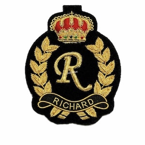 May include: Black embroidered patch with a gold "R" and the name "Richard" on a banner. The patch features a gold crown and laurel leaves, ideal for clothing or craft projects.
