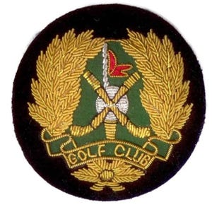 May include: A circular Golf Club patch with a black velvet border. The design includes crossed golf clubs, a red flag, and gold-coloured laurel leaves. The words "GOLF CLUB" are embroidered in gold thread.
