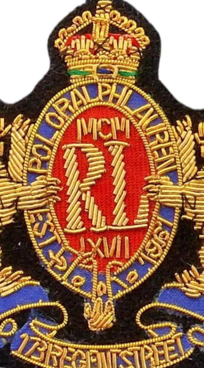 May include: A gold, red, and blue embroidered patch featuring a crown at the top and the text POLO RALPH LAUREN, MCM, RI, LXVII, and 17 REGENT STREET. The design includes intricate gold thread detailing on a black fabric base with a central oval.