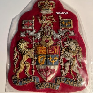 以下が含まれることがあります： 詳細な紋章が刺繍された赤いパッチ。王冠、旗、ライオン、馬のデザインで、「MAGNIFICENTIA ET GLORIA」の文字が入っています。パッチは透明なプラスチックで包まれています。