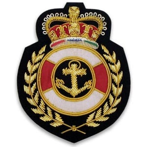 May include: Embroidered navy blue patch featuring a gold anchor within a white and red life preserver design, surrounded by gold laurel leaves. A gold crown with red accents sits atop the design. The patch is a symbol of maritime or naval affiliation.