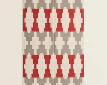 May include: Rectangular rug with a geometric pattern in red, gray, and off-white. The design features repeating shapes, creating a symmetrical and visually appealing textile. The rug is likely made of woven material and suitable for home decor.