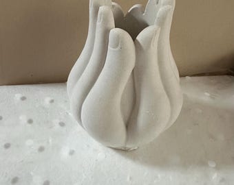 May include: A white, tulip-shaped vase with a unique design. The vase is sculpted to resemble a series of hands, with fingers extending upwards to form the opening. The textured surface adds to its artistic appeal. This decorative piece is ideal for floral arrangements.