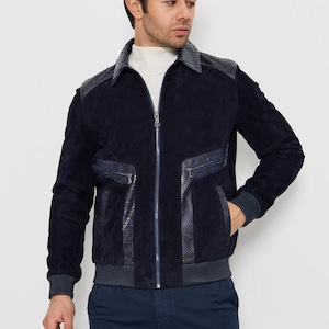 May include: Navy blue suede jacket with a zip-up front, featuring leather accents on the shoulders and pockets. The jacket has a ribbed collar and cuffs, and a matching navy blue ribbed hem. A stylish outerwear piece.