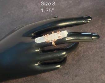 May include: A size 8 ring with a clear, rectangular crystal, measuring 4.4 cm, is wrapped in gold-colored wire. The ring is displayed on a black hand-shaped form against a dark background. The text "Size 8 1.75" is visible.