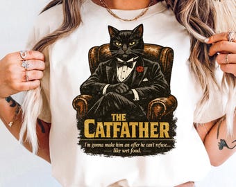 Könnte beinhalten: Ein cremefarbenes T-Shirt mit einer Grafik einer schwarzen Katze im Smoking, die in einem braunen Ledersessel sitzt. Der Text lautet THE CATFATHER und I'm gonna make him an offer he can't refuse... like wet food. Das Motiv ist mittig platziert.