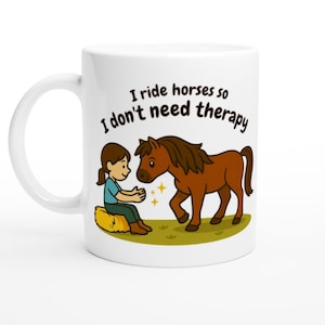 Op de afbeelding: Witte keramische mok met een cartoon illustratie van een meisje en een bruin paard. Het meisje zit op een hooibaal en het paard staat op groen gras. De mok heeft de tekst: "I ride horses so I don't need therapy."
