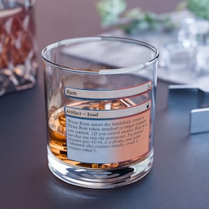 May include: A clear glass tumbler with a printed label that reads "Rum" and "Artifact - Food." The glass is filled with a golden liquid and ice. The text on the label describes the card's effect.