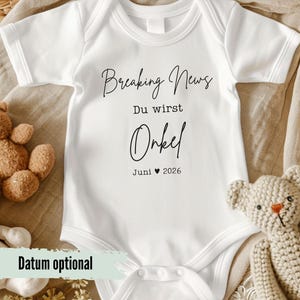 Könnte beinhalten: Weißer Baby-Body mit dem Text "Breaking News Du wirst Onkel Juni 2026" in schwarzer Schrift. Der Body hat kurze Ärmel und einen runden Ausschnitt. Ein Teddybär ist auf der linken Seite des Bodys sichtbar.