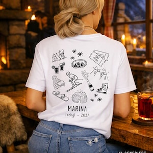 Könnte beinhalten: Ein weißes T-Shirt mit einer schwarzen Strichgrafik auf der Rückseite. Das Design zeigt Symbole wie Skier, Skibrille, Skipass, Skifahrer, Champagnerflasche, Snowboard und Bierkrüge. Der Text lautet MARINA Ischgl - 2027.