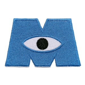 Può includere: Una toppa blu ricamata a forma di lettera "M" con un grande occhio al centro. L'occhio ha un'iride bianca e una pupilla nera. La toppa è probabilmente per abbigliamento o accessori.