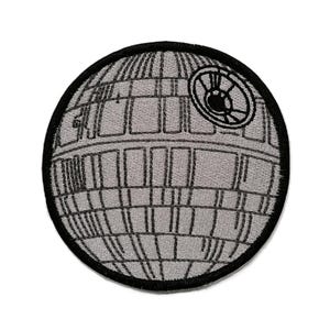 Puede incluir: Un parche bordado circular que presenta un diseño de estación espacial esférica gris con líneas de cuadrícula cosidas en negro y un detalle de disco cóncavo circular prominente en el lado superior derecho, todo dentro de un borde negro grueso.