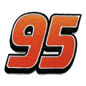 Puede incluir: Parche bordado naranja con el número 95, contorneado en negro y con un borde blanco. El número tiene una apariencia texturizada, lo que sugiere una construcción de tela o hilo. El parche está probablemente diseñado para su aplicación en ropa o accesorios.