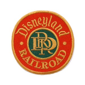 May include: A circular embroidered patch featuring a red background with a gold border. The text Disneyland Railroad is stitched in gold lettering around a central green circle containing the gold interlocking letters DRR.