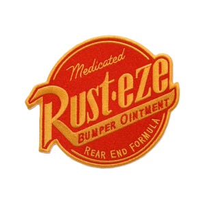 Può includere: Una toppa ricamata circolare con sfondo rosso e testo giallo. Il testo recita Medicated Rust-eze Bumper Ointment Rear End Formula. Il design presenta un bordo giallo e scritte stilizzate con una R e una E prominenti.