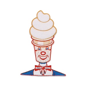 Könnte beinhalten: Ein gestickter Aufnäher, der eine Softeis-Charakterfigur mit lächelndem Gesicht zeigt. Die Waffel hat ein Waffelmuster, rote Gesichtszüge und eine rote Fliege, auf der der Schriftzug "Miles Standish" in blauer Schreibschrift zu sehen ist.