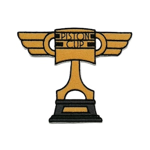Pode incluir: Um emblema bordado em forma de troféu dourado com asas em ambos os lados. O centro do troféu apresenta o texto PISTON CUP em letras pretas. A base do troféu é preta e todo o design é contornado por uma fina borda de cor branca.