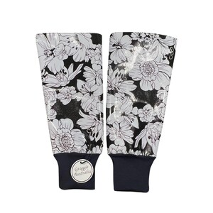 May include: Two black and white floral print arm sleeves. The sleeves feature a repeating pattern of large white flowers on a black background. The cuffs are navy blue, and each sleeve has a small, round tag that says "Graggie Australia."