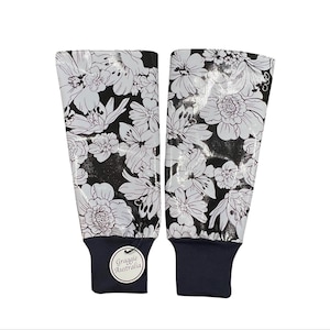 May include: Two floral-patterned arm sleeves. The sleeves feature a black background with white flowers. The cuffs are navy blue. The brand name "Graggie Australia" is printed on a white tag attached to one of the sleeves.