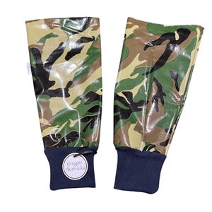 May include: A pair of green, brown, and black camouflage print arm warmers with black elastic cuffs. The arm warmers have a shiny, almost wet look. A white tag with the text "Graggie Australia" is attached to one of the arm warmers.