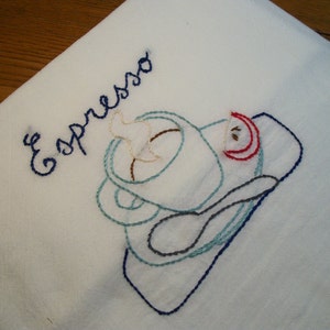 May include: White embroidered kitchen towel with the word "Espresso" in dark blue script. The design features a coffee cup, saucer, and spoon, all outlined in shades of blue, brown, and red.