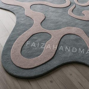 Pu&ograve; includere: Un tappeto astratto grigio e rosa con un design unico e fluido. Il tappeto presenta una base grigia con un motivo organico rosa chiaro. Il testo "FAIZAHANDMADE" &egrave; sottilmente integrato. Il tappeto &egrave; posato su un pavimento in legno.