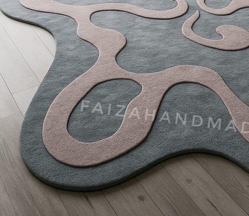 Pu&ograve; includere: Un tappeto astratto grigio e rosa con un design unico e fluido. Il tappeto presenta una base grigia con un motivo organico rosa chiaro. Il testo "FAIZAHANDMADE" &egrave; sottilmente integrato. Il tappeto &egrave; posato su un pavimento in legno.