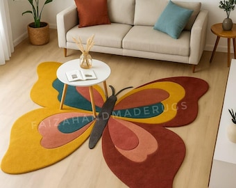 Puede incluir: Una alfombra grande en forma de mariposa con un diseño amarillo, turquesa, naranja y marrón. La alfombra está colocada sobre un suelo de madera en un salón, con un sofá, una mesa de centro y una mesa auxiliar visibles en el fondo. El texto "FAIZAHANDMADERUGS" es visible en la alfombra.